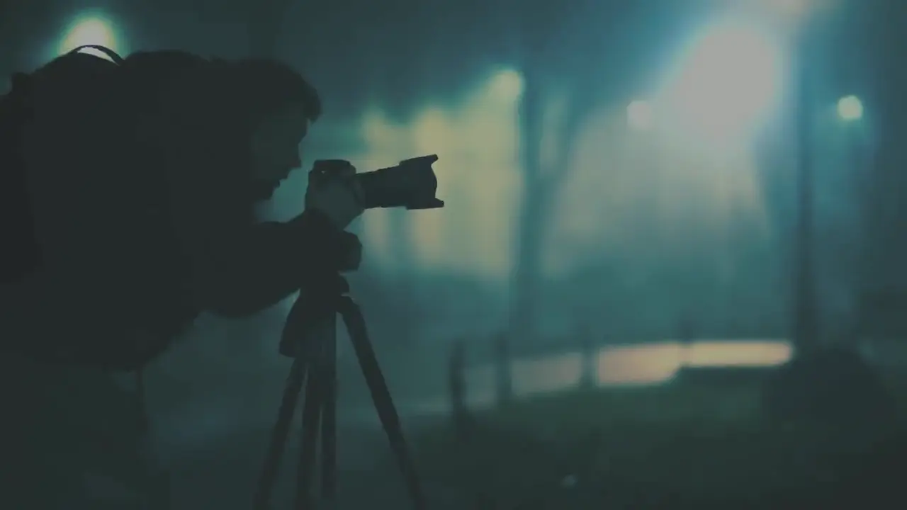 A camera operator silhouetted behind a camera on a tripod at night